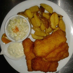 Fish and chips servido con papas fritas, salsa tartara y ensalada de repollo