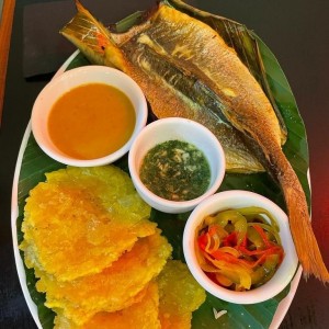 Corvina en Bijao con Tamal en Olla, Patacones, Salsa al Ajillo y Encurtidos 