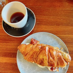 Cafe geisha y croissant de bacon con queso