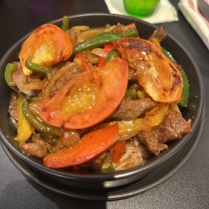 Salteado de res con cebolla y tomates asados sobre un tamal de arroz con frijoles rojos